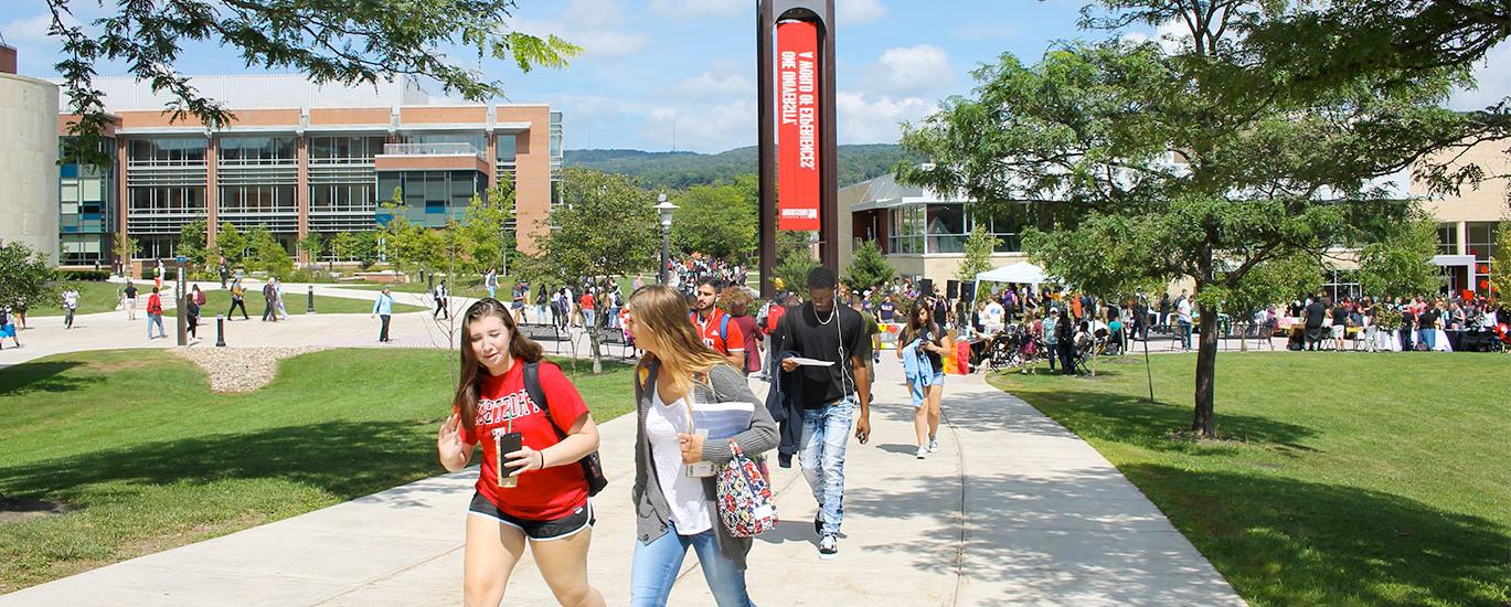 A large group of Frostburg State students walk to class near the campus clocktower on a warm, 阳光灿烂的日子