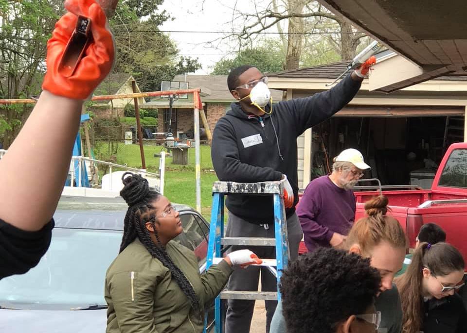 group of students volunteering by painting a house