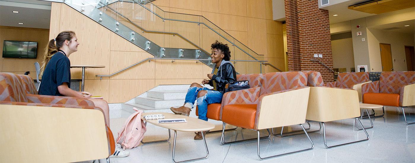 Two students sit and have a conversation on the bottom floor of the Gira Center